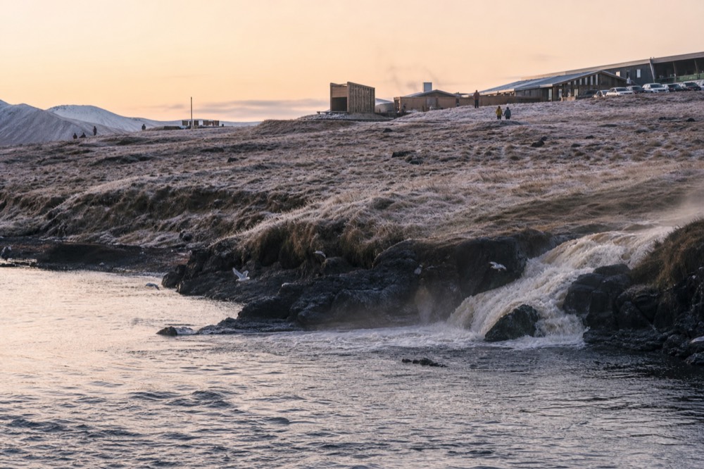 Warm water meeting the ocean along a rocky black shoreline