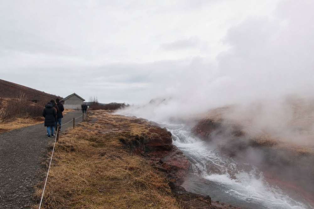 Steam rising from hot springs beside a powerful water flow in a rural setting