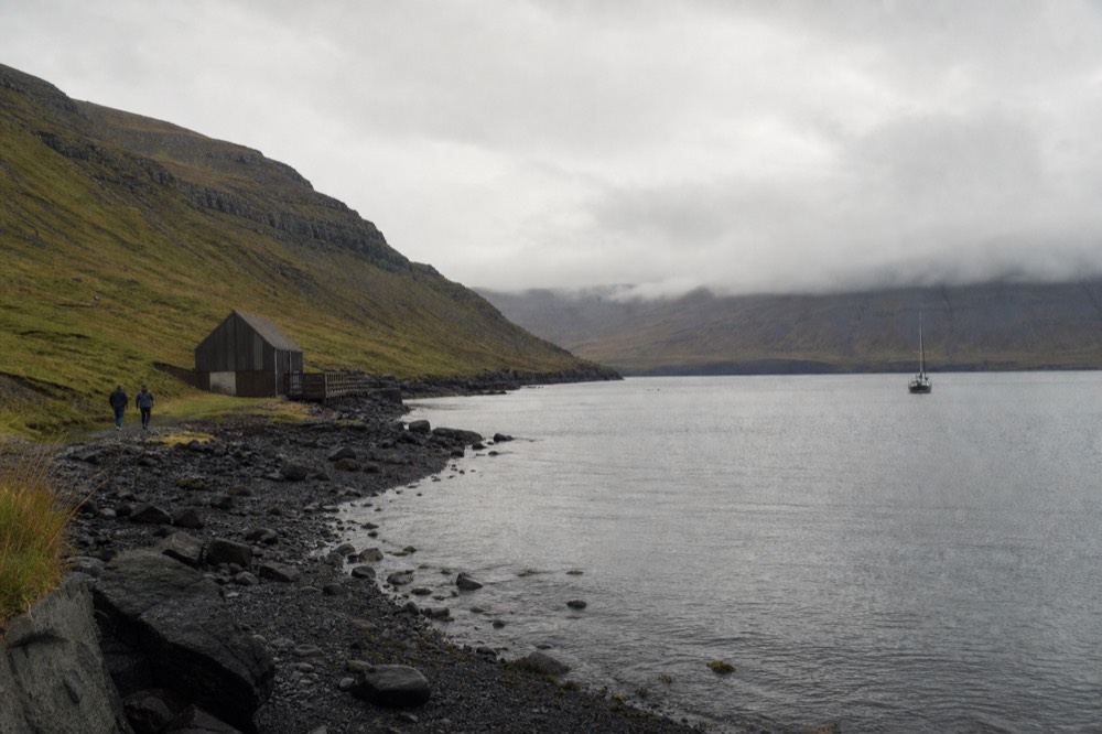 A wide fjord landscape with still water and low clouds over dark hills