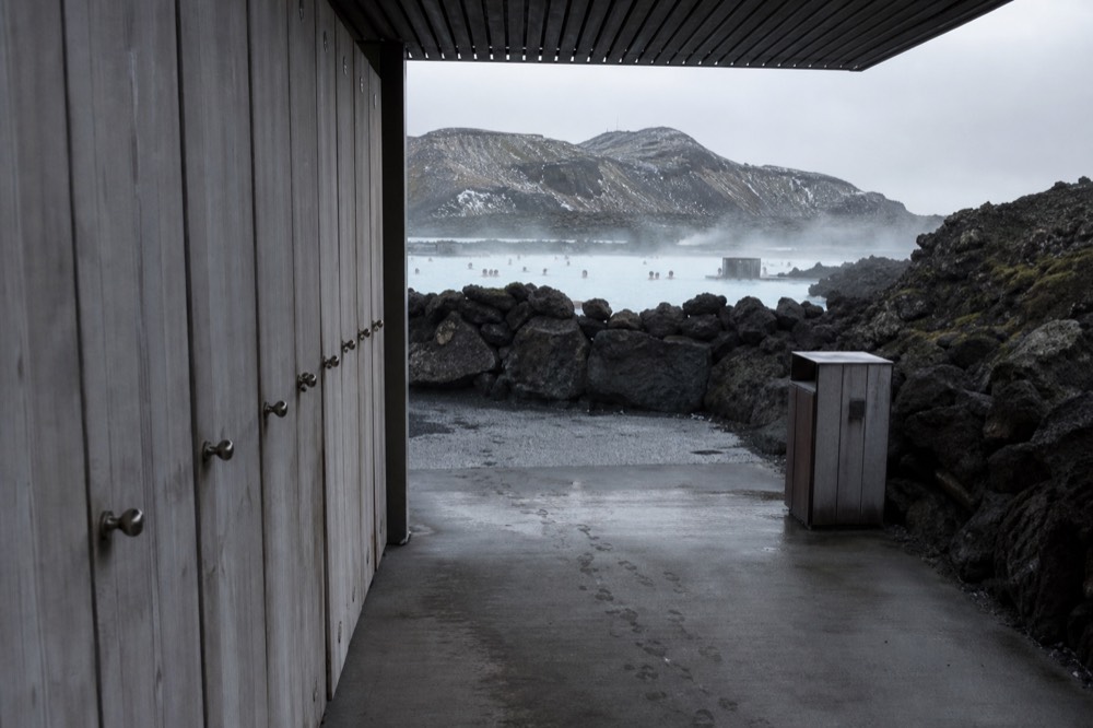 A lagoon entrance with a sign listing ticket tiers and a view of steaming pools beyond