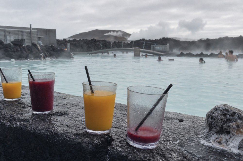 A swim-up bar counter with glasses of colorful drinks lined up beside a geothermal pool
