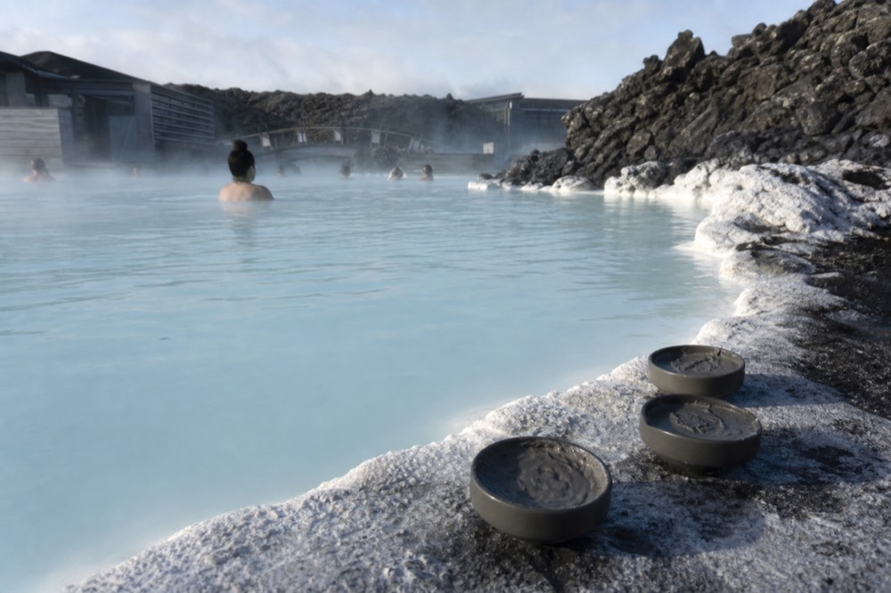 A close-up of the Blue Lagoon's milky blue water with silica mud mask pots on the edge