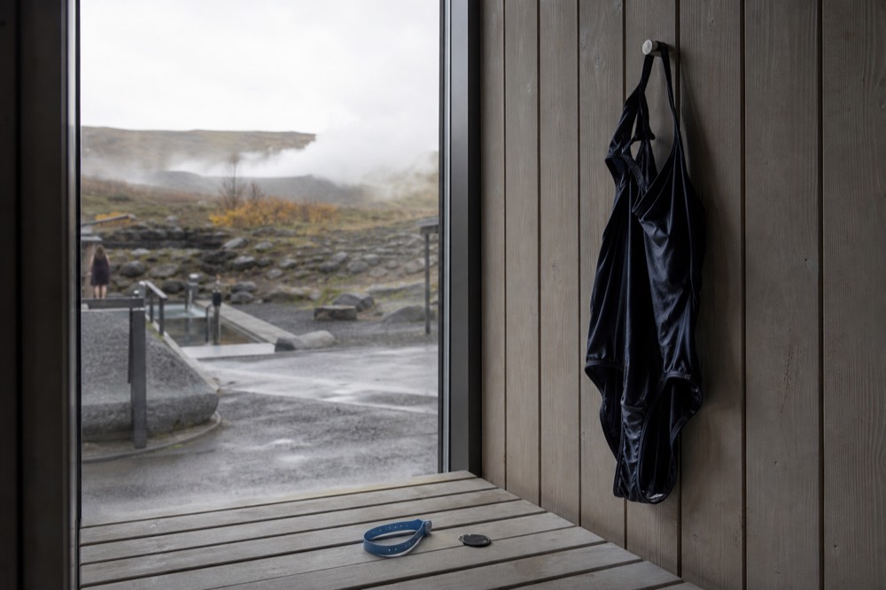 A waterproof wristband lying on a wooden bench beside a locker key in a lagoon changing room
