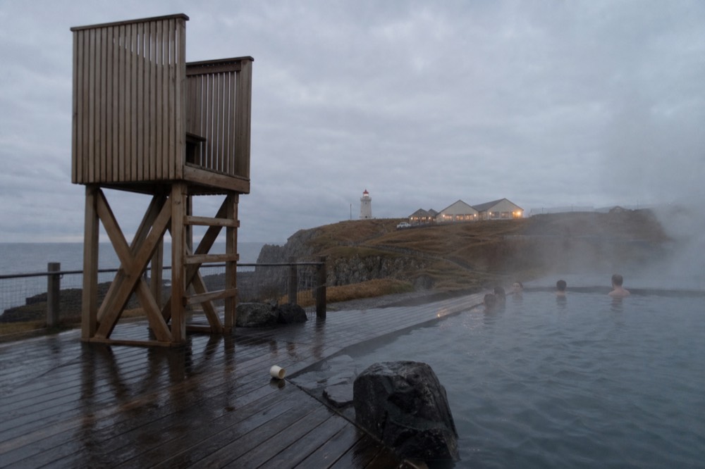 A lifeguard chair and signage beside a steaming geothermal pool in evening light