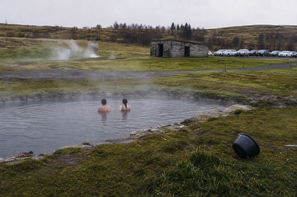 A natural hot pool ringed by grass and steaming vents in a geothermal area