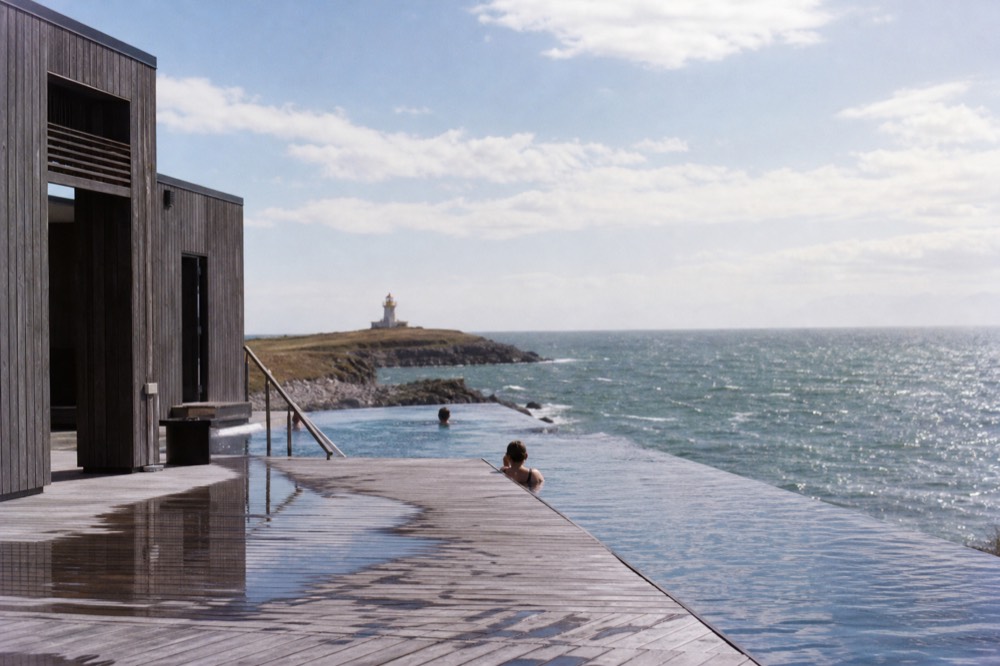 A modern spa building with a long infinity edge overlooking a cold sea