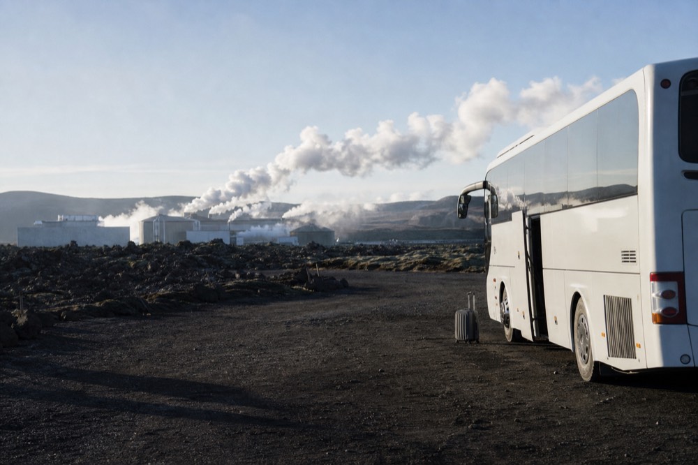 A coach parked beside a geothermal power station and steam plumes on a lava plain