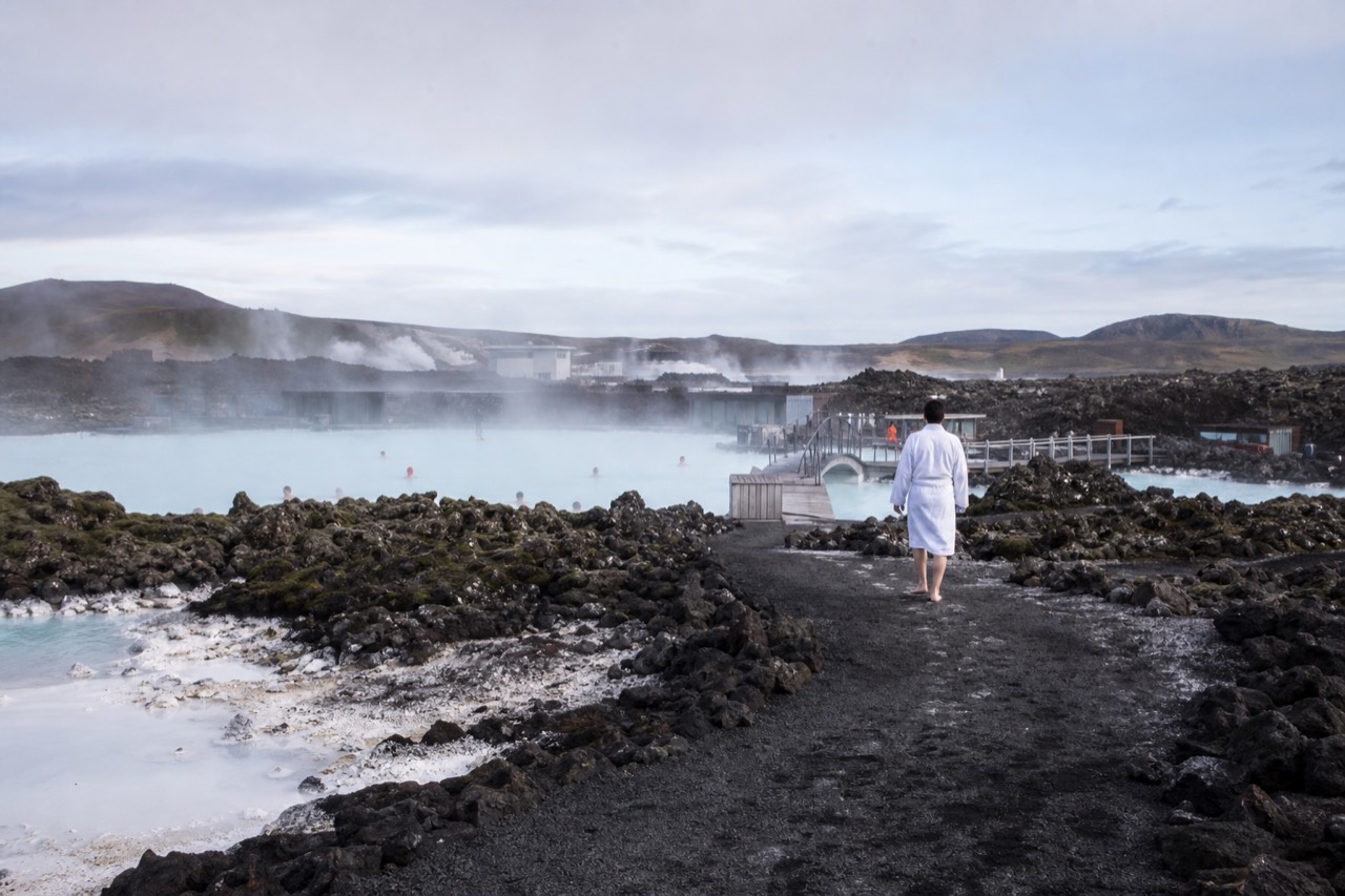 Steam rising from a geothermal lagoon beside dark volcanic rock under a pale sky