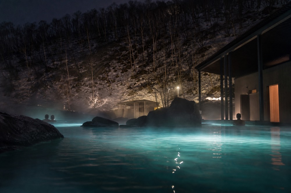A geothermal pool glowing with steam beside a dark mountain landscape at night