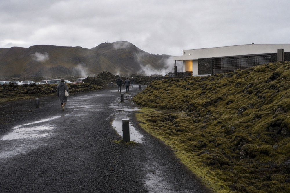 A geothermal spa building on a flat lava plain with distant volcanic ridges under cloud