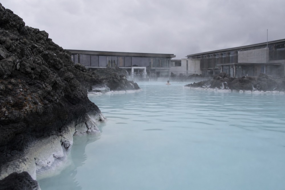 A calm geothermal pool reflecting a pale sky between dark rock formations