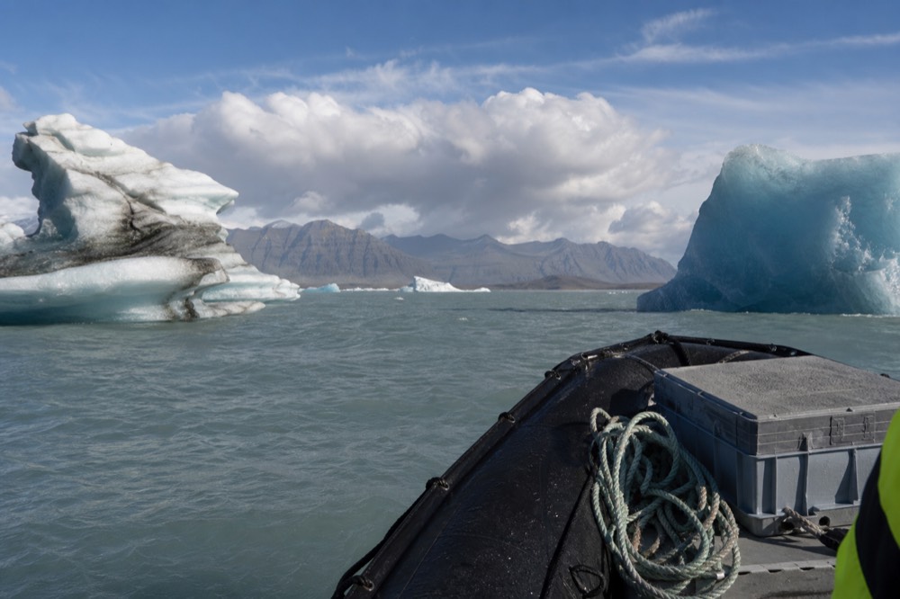 A rigid inflatable boat moving between large blue icebergs on open water