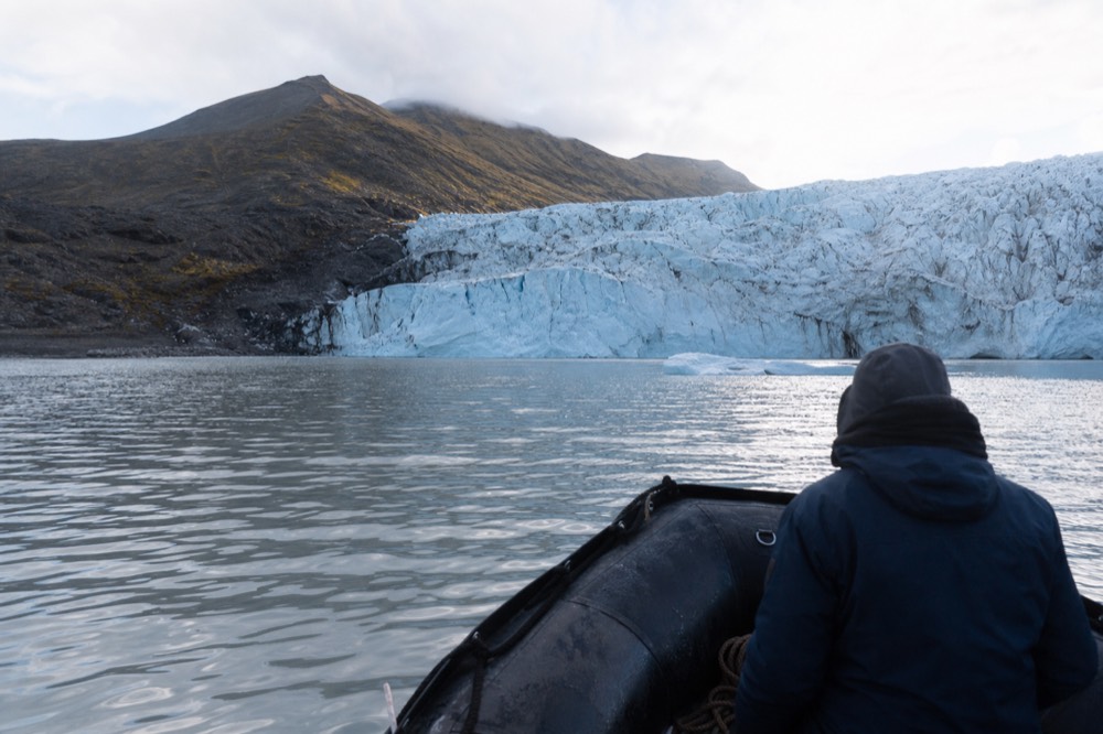 A small boat approaching a tall wall of glacier ice at close range