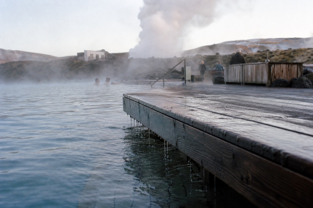 A wooden deck edge meeting warm blue water with steam in the background