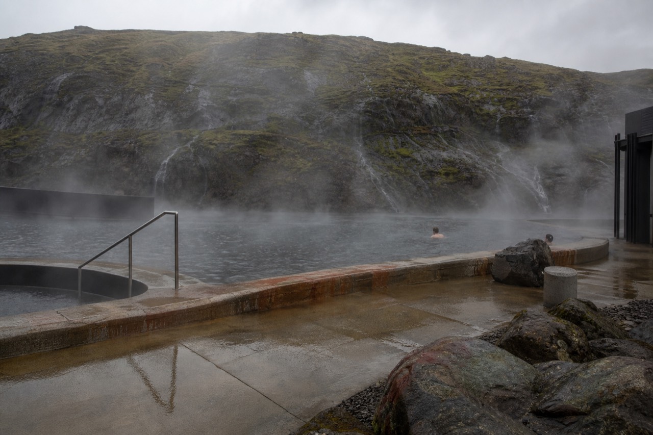 Steam rising from geothermal pools beside a mossy rock face in rural West Iceland
