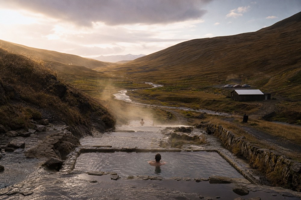 Terraced geothermal pools with steam rising above a green river valley