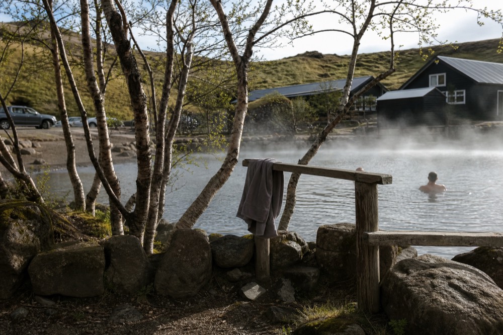 Steam rising from a rock-walled pool surrounded by birch trees