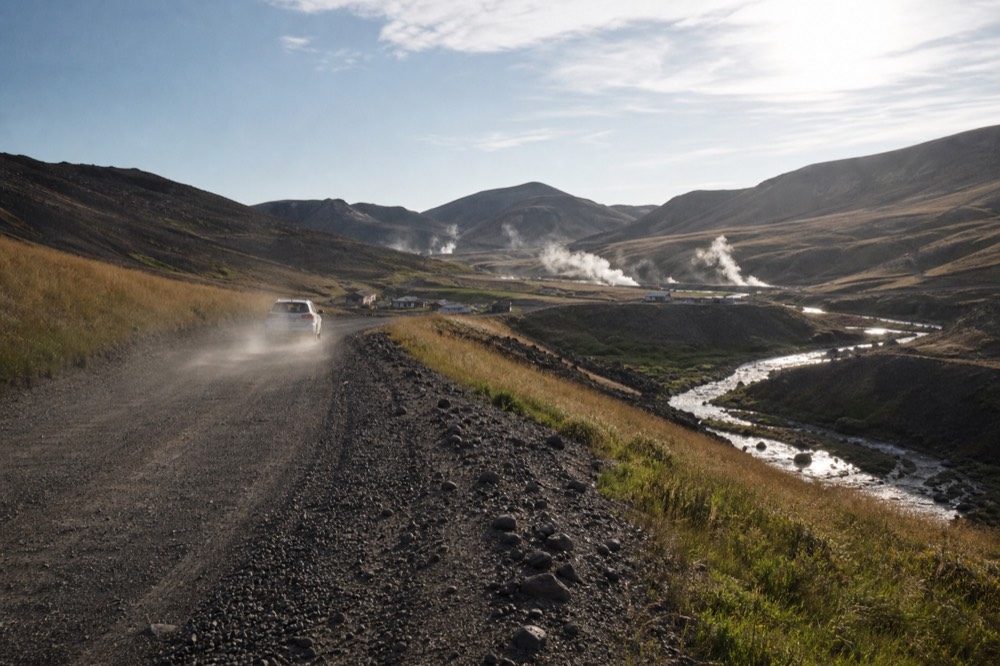 Quiet rural road curving past geothermal fields toward a small village