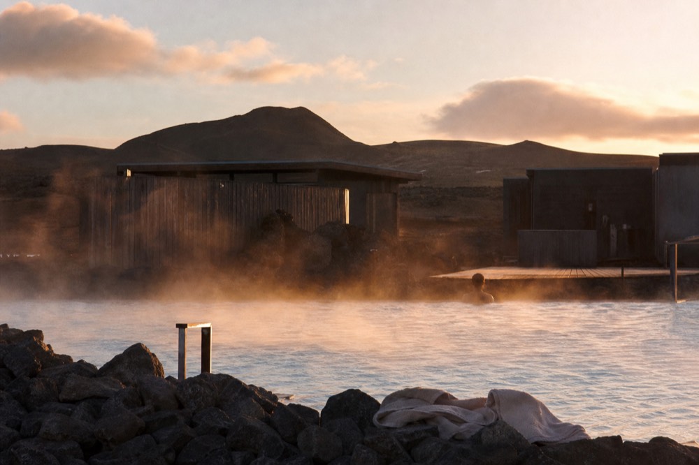 Steam rising from an outdoor pool in low evening light with hills behind