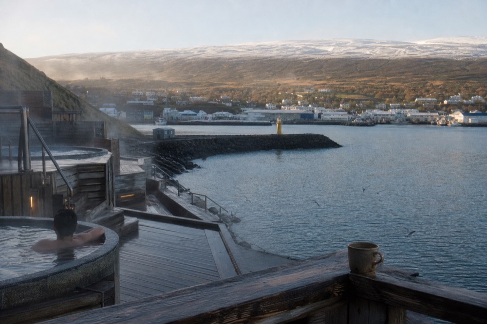 A steaming lagoon terraced into a hillside with a view over a northern fjord town