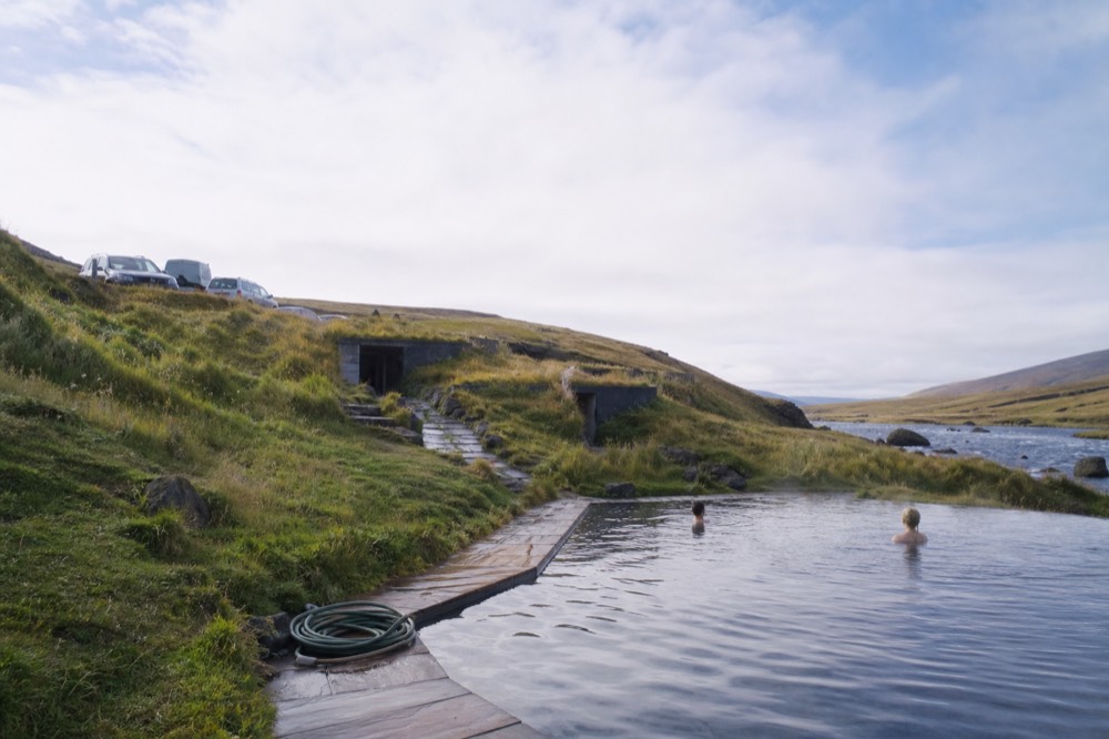 A modern geothermal pool built into a grassy riverbank under a wide sky