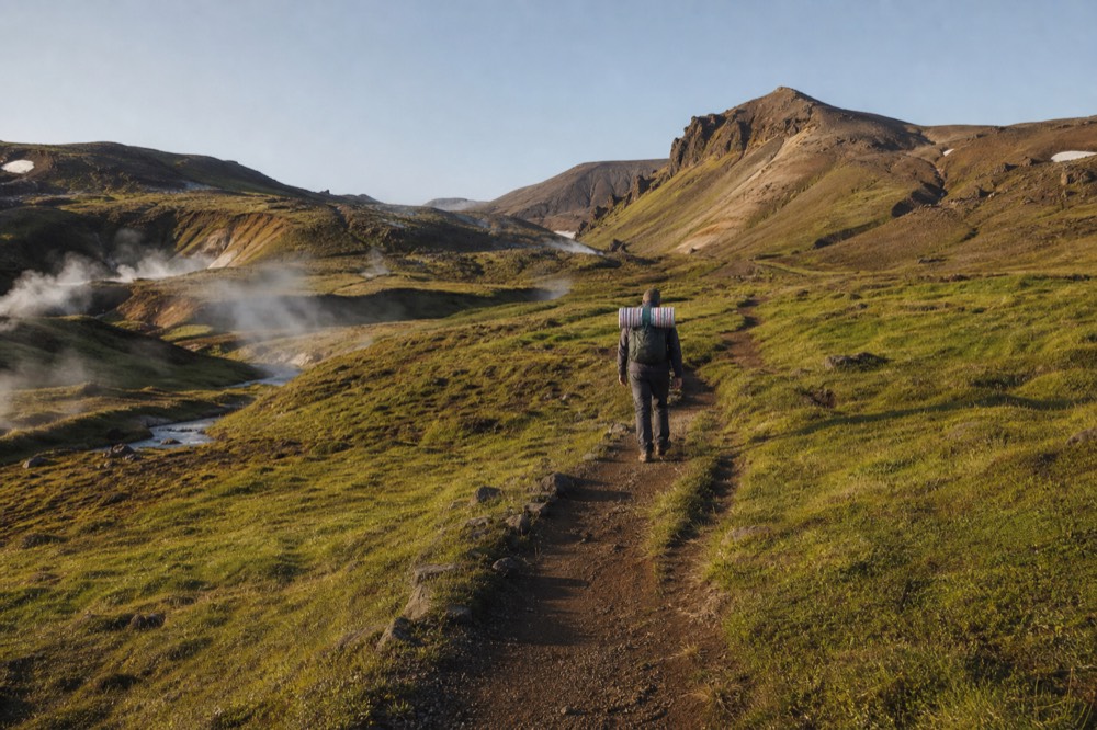A hiker's path winding up a steaming green valley toward distant hills