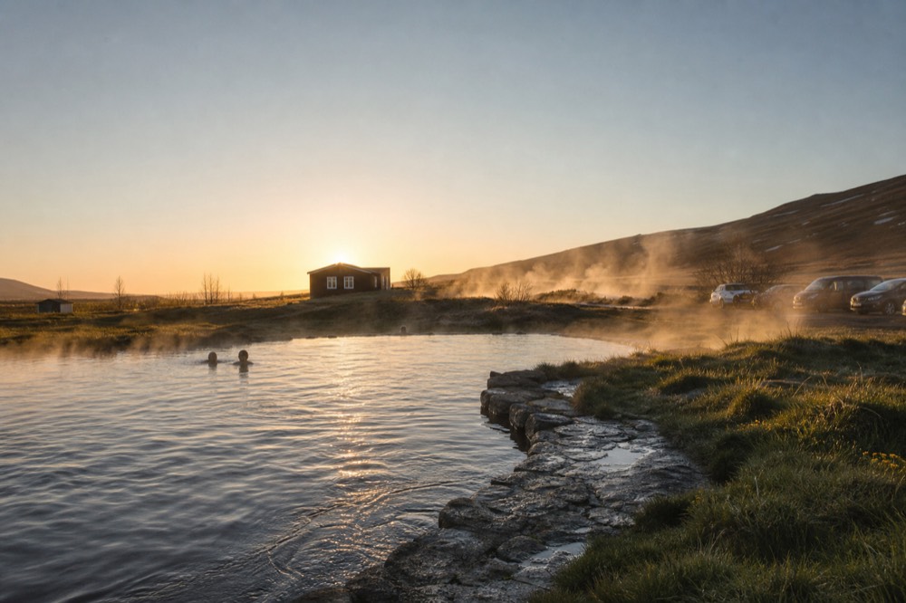 Steam drifting from a natural pool across a geothermal field in evening light