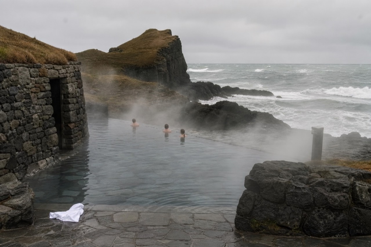 Steam rising from a geothermal lagoon at the edge of a dark coastline