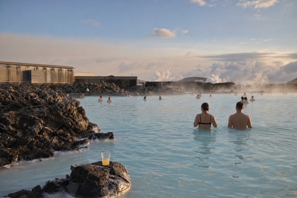 Bathers waist-deep in a large steaming turquoise lagoon edged with black lava