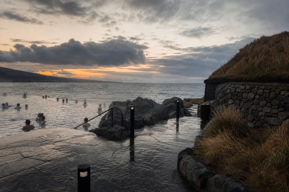 An infinity-edge geothermal pool overlooking a dark ocean horizon at dusk