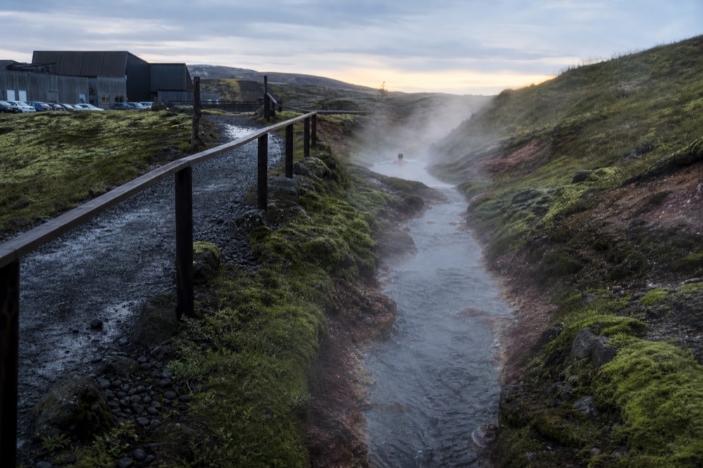 Steam drifting off a narrow geothermal channel between mossy rocks at dusk