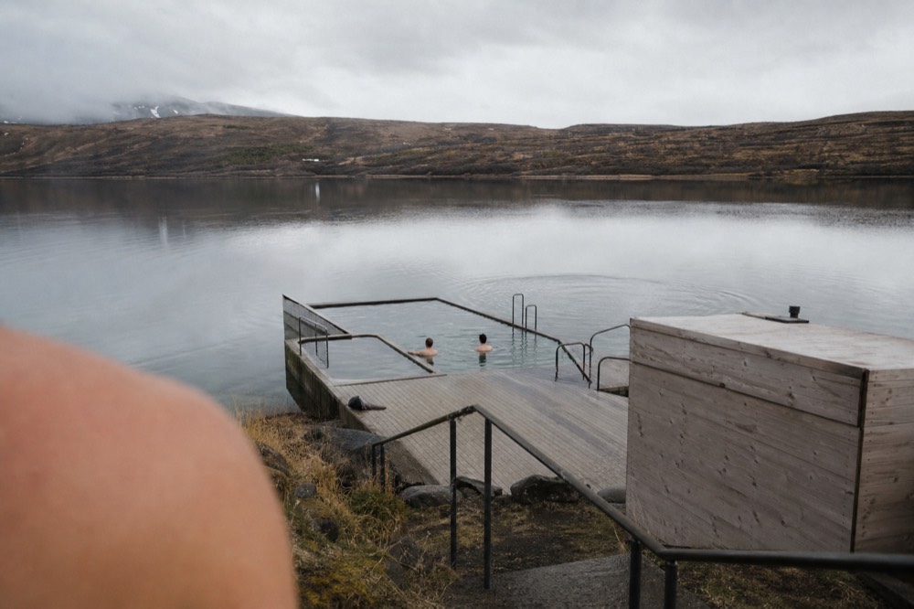 Geothermal pools extending over a calm lake surrounded by low hills