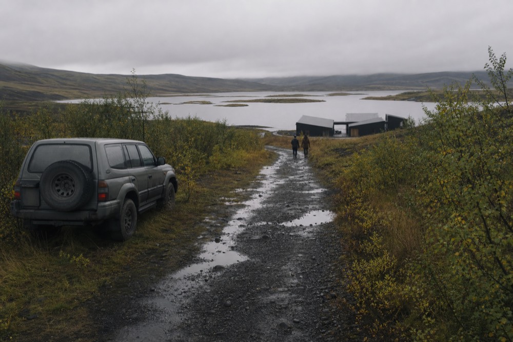 A gravel path leading from a country road toward lakeside geothermal pools