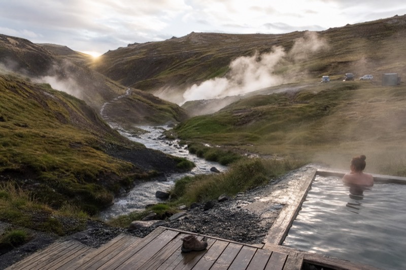 A geothermal pool in south Iceland near the Golden Circle, steam rising over grassy banks with a low ridge behind it.