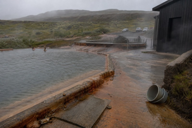 A hot spring lagoon in west Iceland set among fjord scenery, calm grey water and dark hills under soft light.